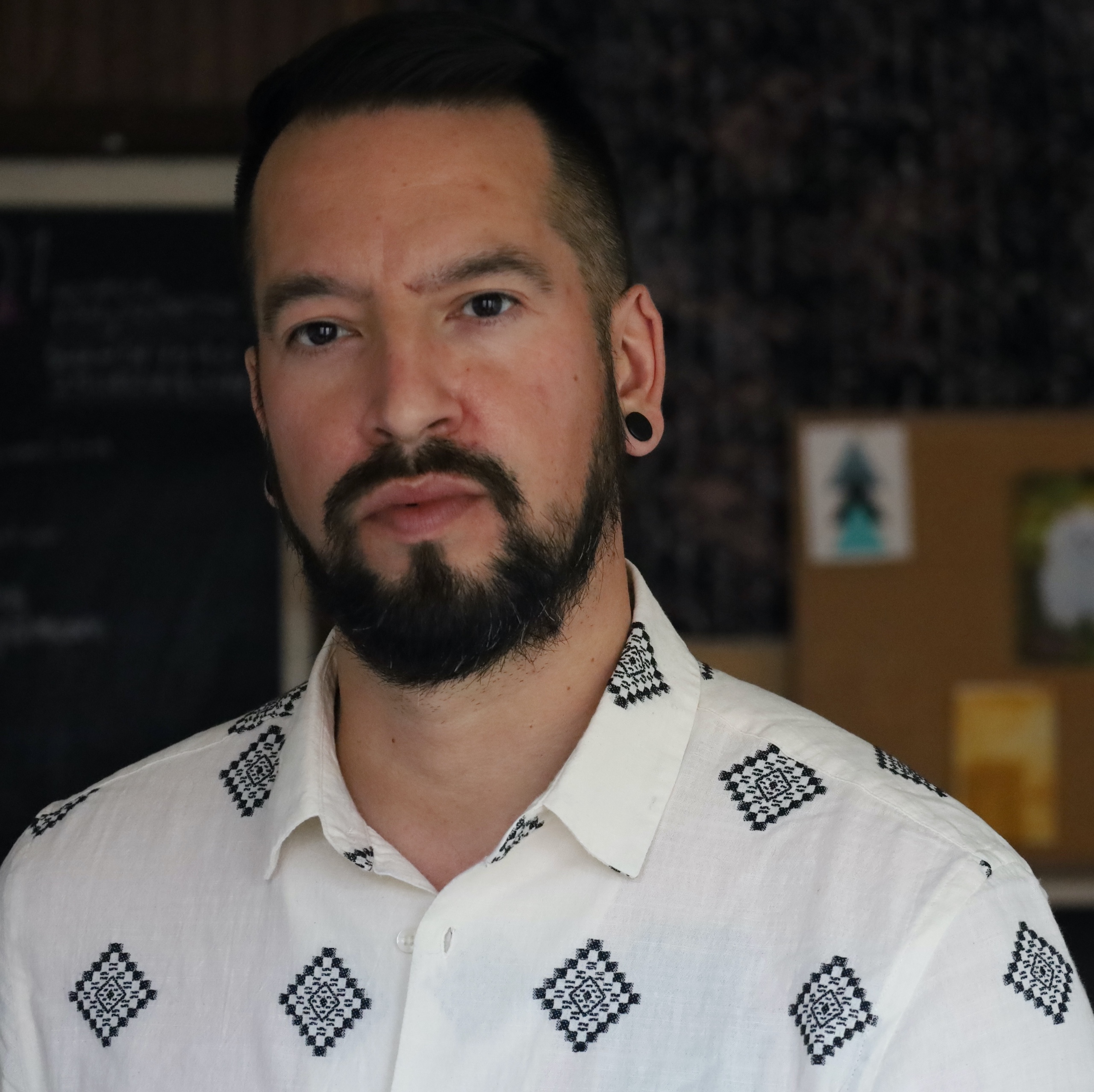James Dixon [ID: James Dixon looking at camera, has dark hair, a beard and is wearing an white button up shirt]