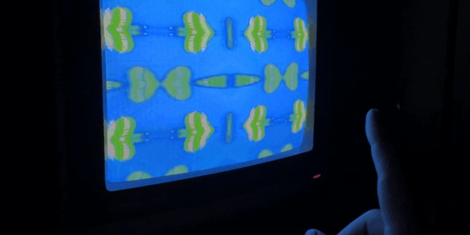 TV monitor screen with a blue background and green and white heart-like shapes, mirrored from the centre of the screen