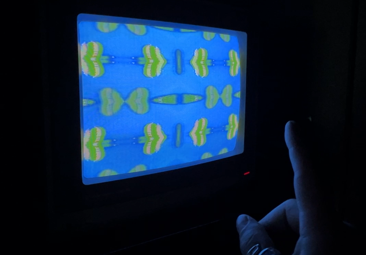 TV monitor screen with a blue background and green and white heart-like shapes, mirrored from the centre of the screen