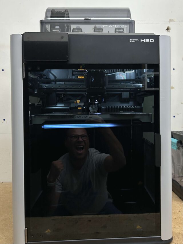 A front shot of a Bambu Labs H2D, with a reflection of Eusebio in the glass