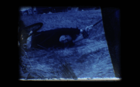 Tinted blue photo of a woman being dragged through grass with a rope around her hands