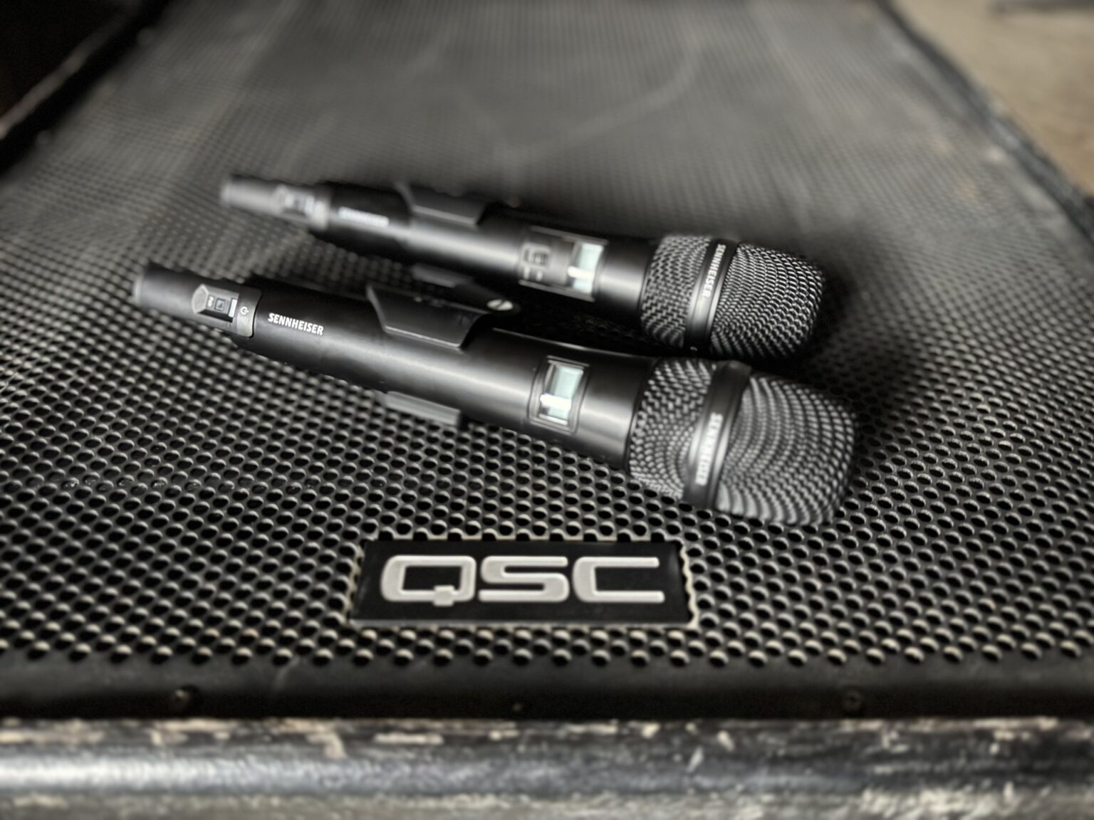 Two wireless Sennheiser mics sit on top of the grill of a QSC sub