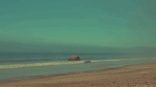 Scenic view of a beach with blue-green sky and a boulder in the water