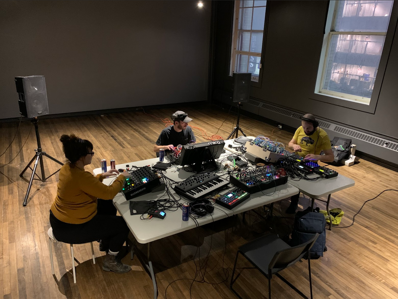 3 people sitting around a table playing samplers and computers.