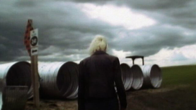 Woman standing in front of large industrial tubing with her back toward the camera
